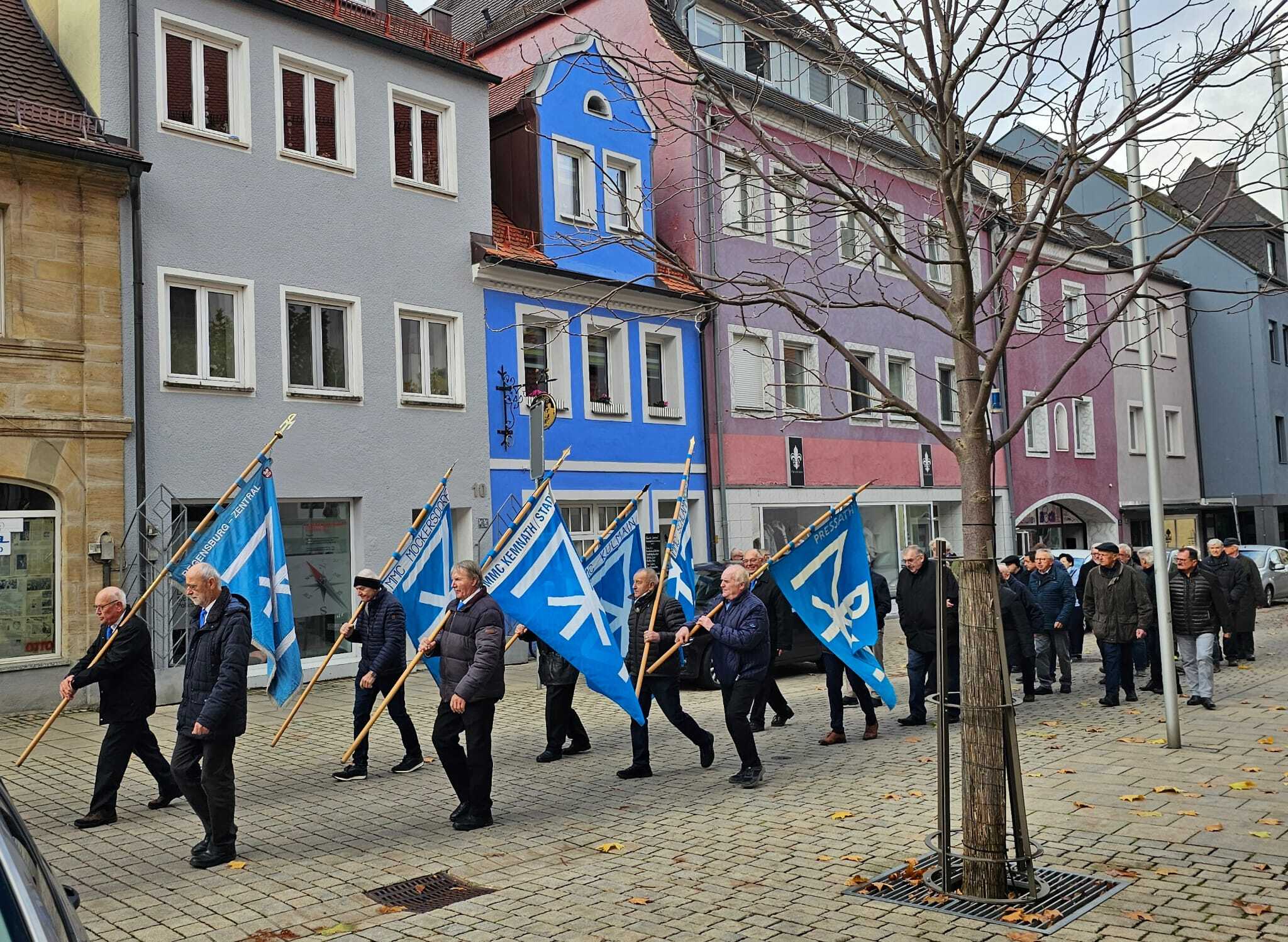 Sodalen mit wehenden Fahnen bei böigem Wind zu den Klängen der Blasmusik und großem Orgelgeläute
