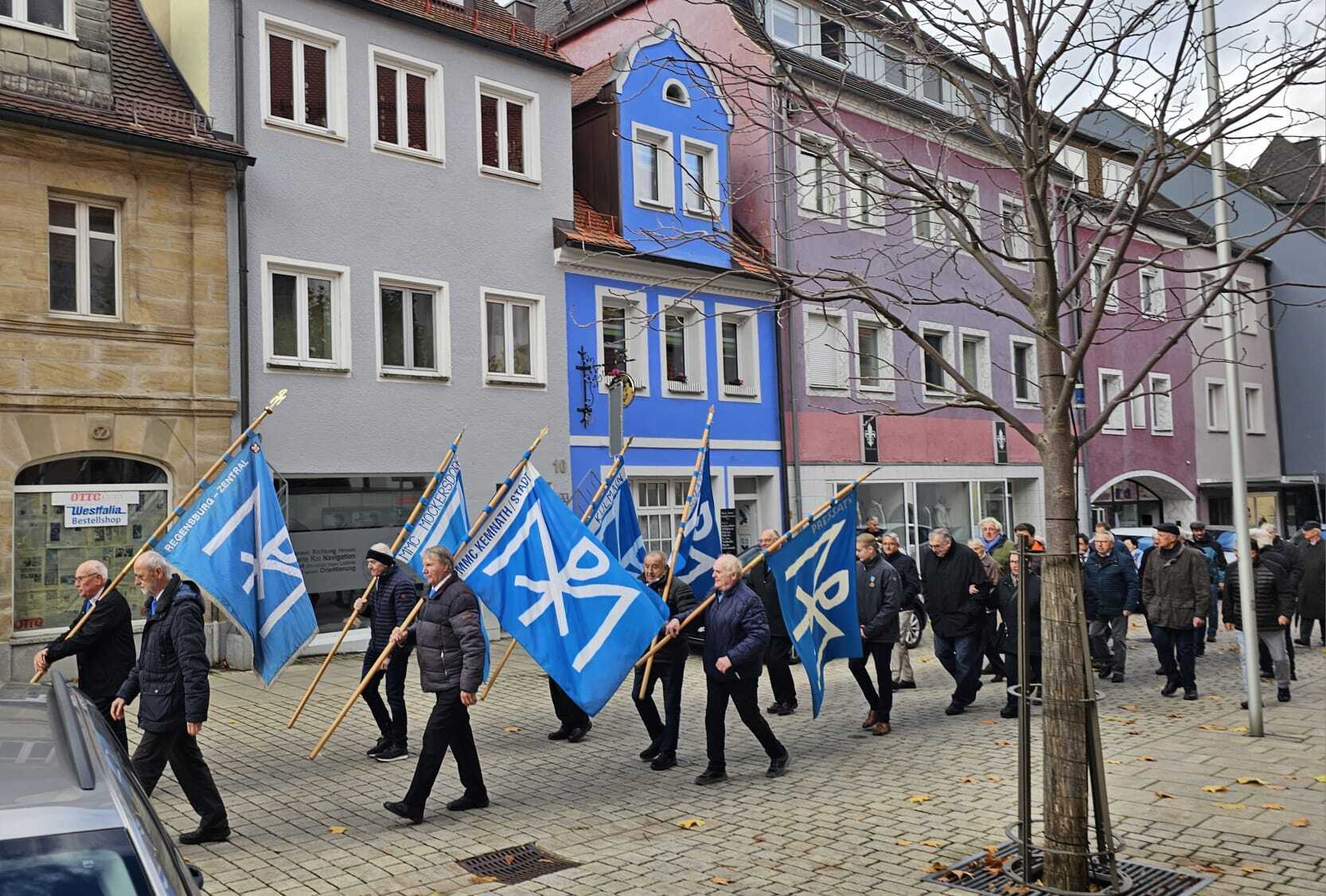 Sodalen mit wehenden Fahnen bei böigem Wind zu den Klängen der Blasmusik und großem Orgelgeläute